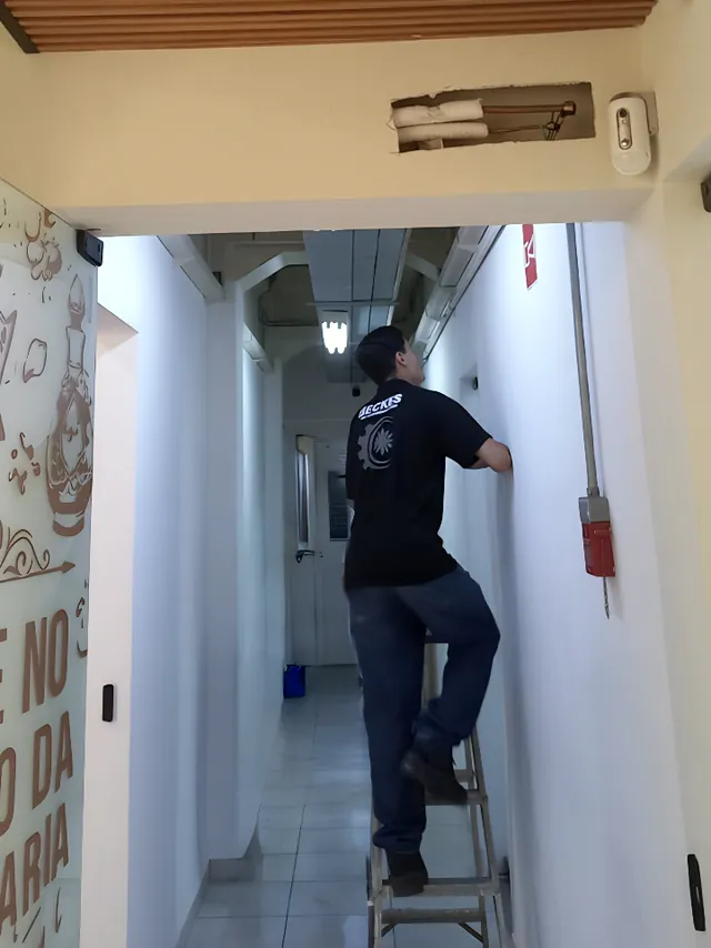 Técnico em uma escada trabalhando no corredor de um estabelecimento comercial