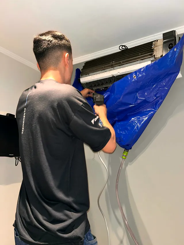 Técnico higienizando a evaporadora com bolsa coletora azul presa ao aparelho